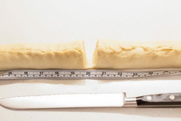  Вид сбоку на тесто для обеденного рулета «Львиный домик», разрезанное посередине с измерительной лентой перед ним. 